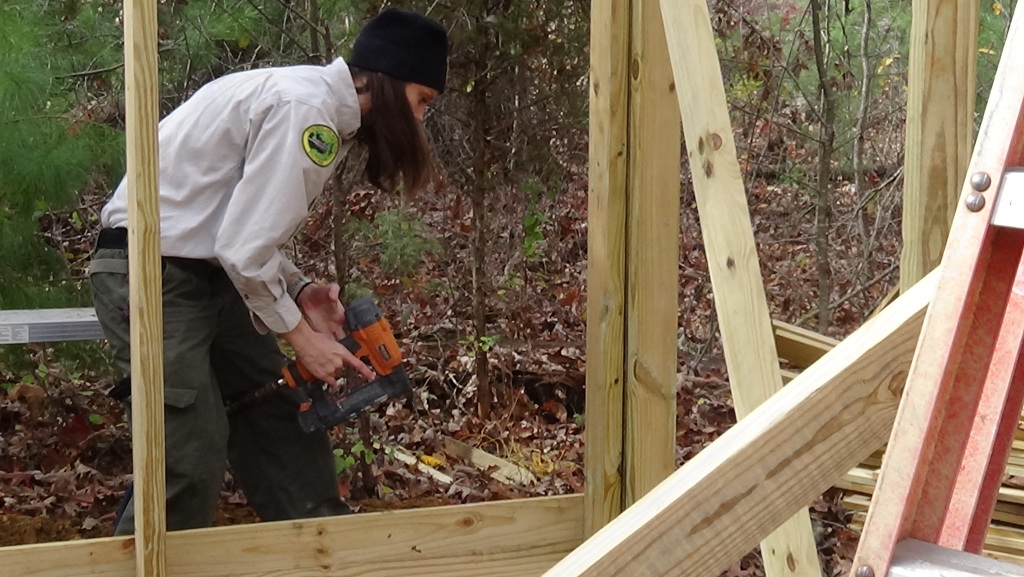 On Nov. 8, Park Ranger Monica Johnson uses a nail gun to install dividing walls to the birds of prey aviary at Cumberland Mountain State Park. (Photo by Diahan Krahulek / Full Sail University)